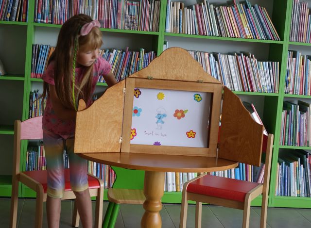 dziewczynka pokazuje ilustracje w teatrzyku kamishibai