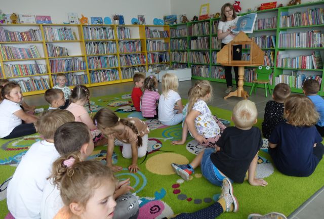 przedszkolaki siedzące na kolorowym dywanie i glądające teatrzyk kamishibai