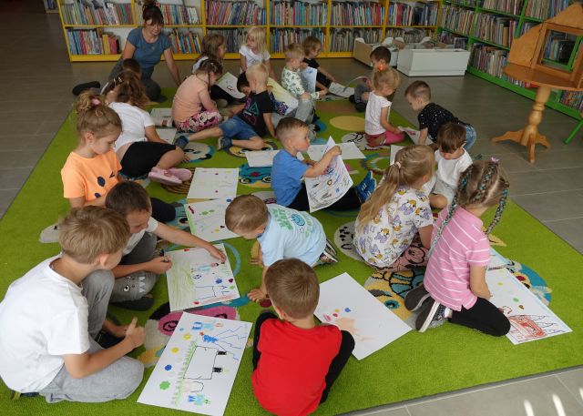 przedszkolaki siedzące na kolorowym dywanie i rysujące na kartkach