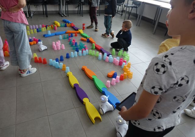 kolorowe kubeczki ułożone na podłodze w taki sposób że tworzą tor przeszkód dla robotó photon, dzieci sterują robotami używając tabletów