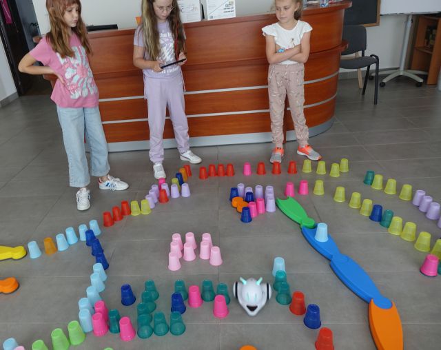 kolorowe kubeczki ułożone na podłodze w taki sposób że tworzą tor przeszkód dla robotó photon, dzieci sterują robotami używając tabletów