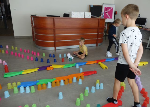 kolorowe kubeczki ułożone na podłodze w taki sposób że tworzą tor przeszkód dla robotó photon, dzieci sterują robotami używając tabletów