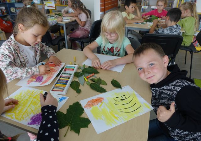 Dzieci przy stolikach malują kredkami
