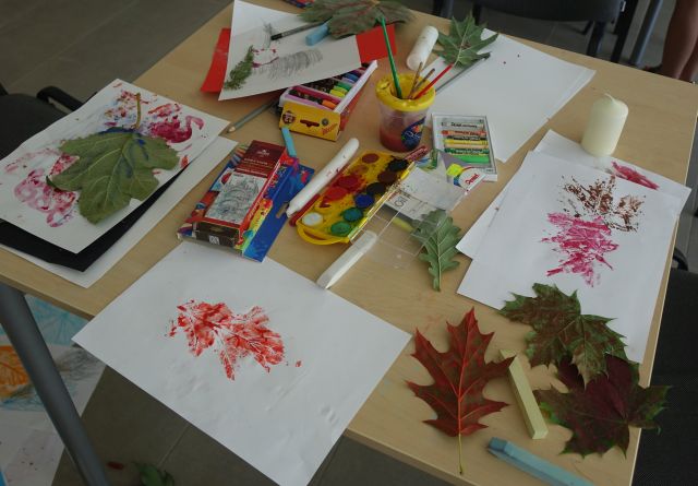 ilustracje liści, na stolikach leżą też farbki, kredki i liście