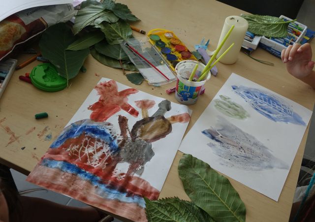 ilustracje liści, na stolikach leżą też farbki, kredki i liście