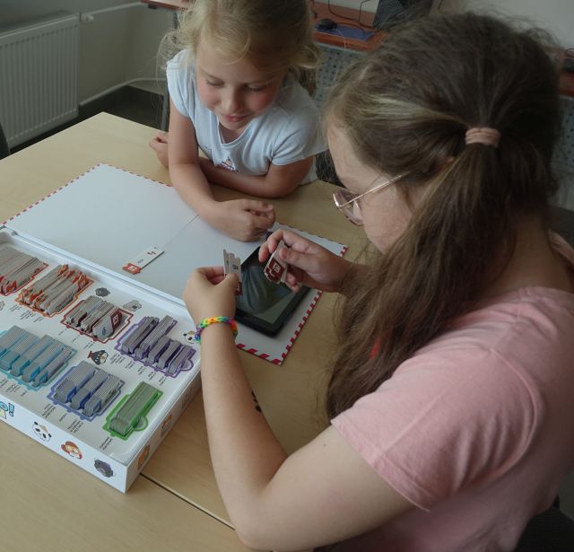 dwie dziewczynki grają w grę planszową używając do kodowania tablet