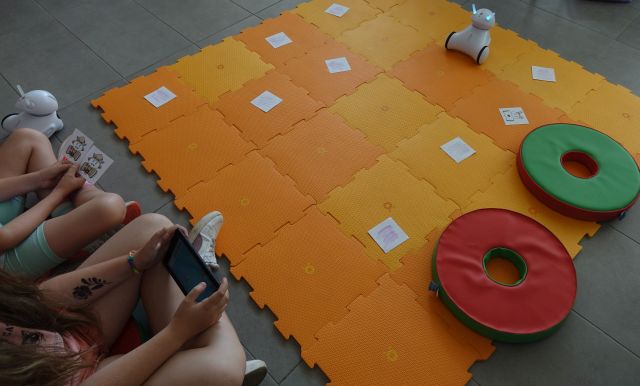 dwie dziewczynki sterują robotami na macie za pomocą tabletów