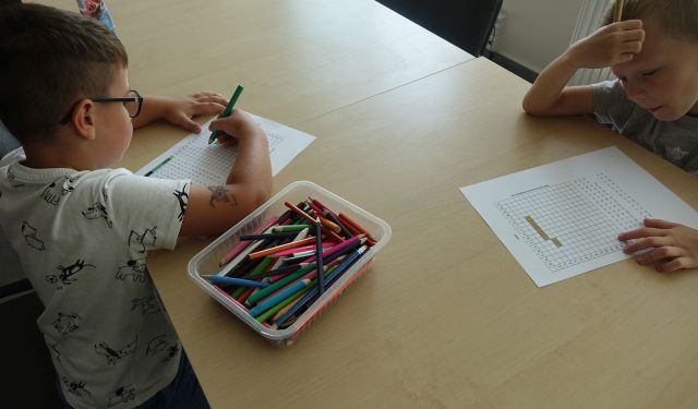 dwóch chłopców zamalowuje kratki na kartkach