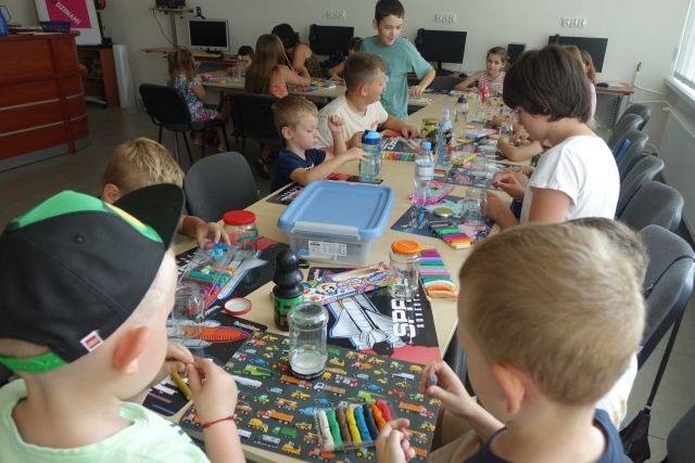 dzieci siedzą przy stołąch, na których leżą plasteliny, słoiki, kartki