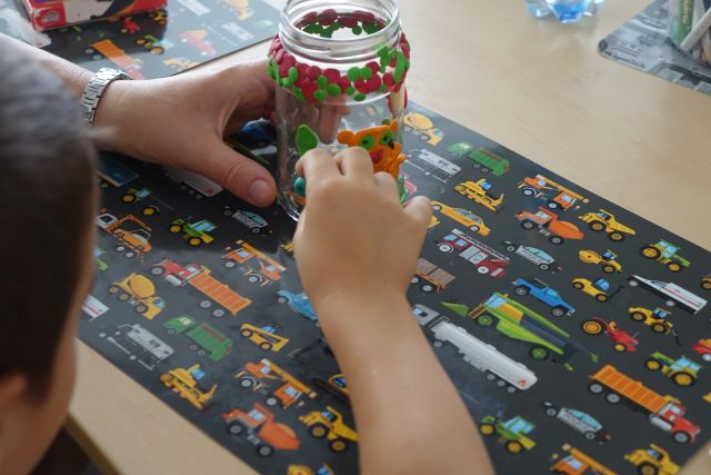 ręce dziecka wyklejające plasteliną słoik