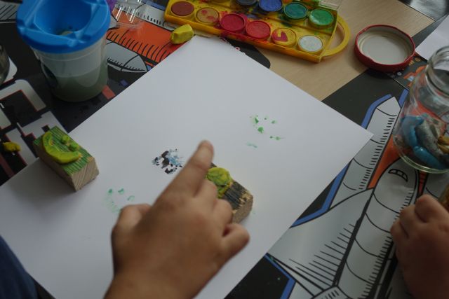 dziecko robi pieczątki plasteliną przyklejoną do kawałków deseczek