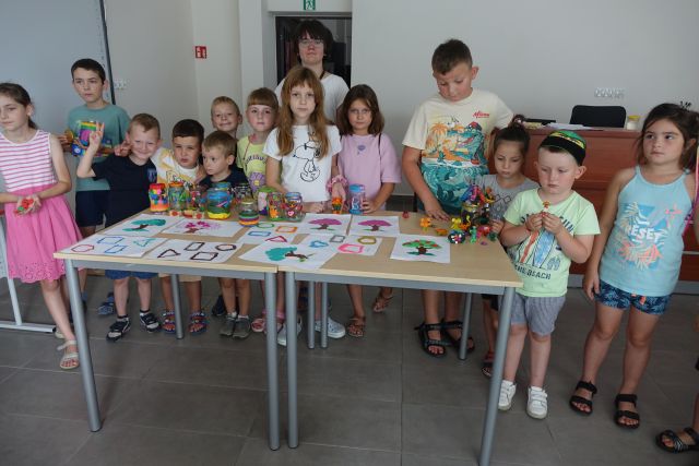 dzieci pozują do zdjęcia, przed nimi na stole wystawione wykonane przez nie plastusie z plasteliny, wyklejanki i wyklejone plasteliną słoiki
