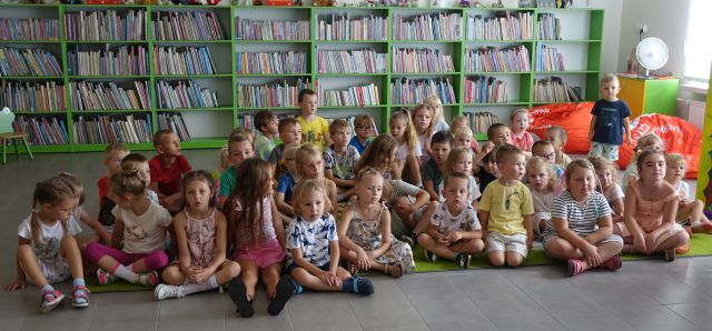 przedszkolaki siedzą na kolorowym dywanie, w tlr regały z książkami