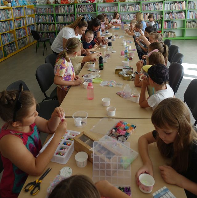 dzieci siedzą przy stołach, na których leżą kolorowe koraliki