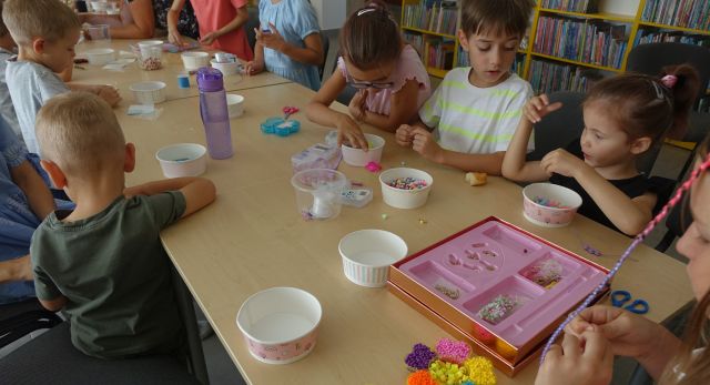 dzieci siedzą przy stolikach i robią branzoletki z kolorowych koralików