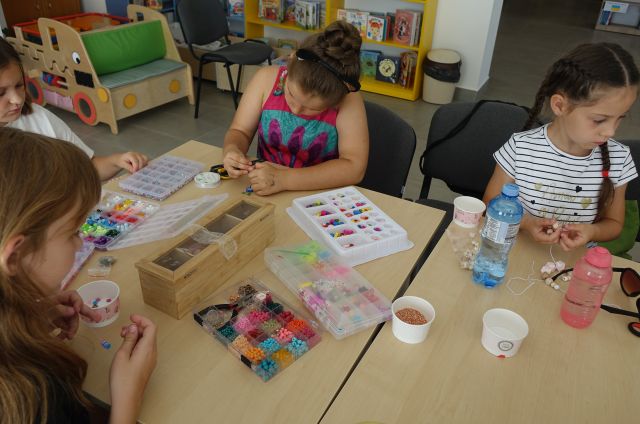 dzieci siedzą przy stolikach i robią branzoletki z kolorowych koralików