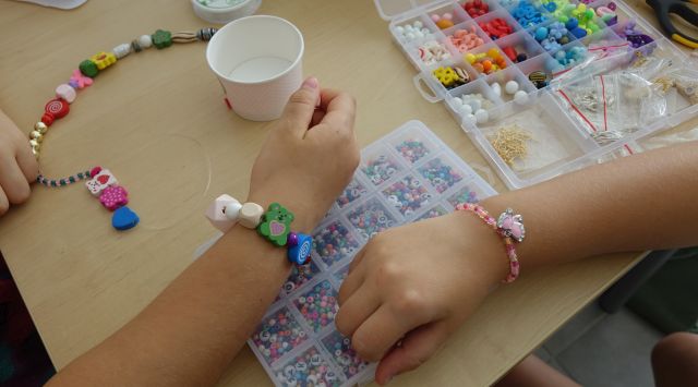 dwie rączki dziecięce prezentują wykonane przez siebie branzoletki z kolorowych koralików
