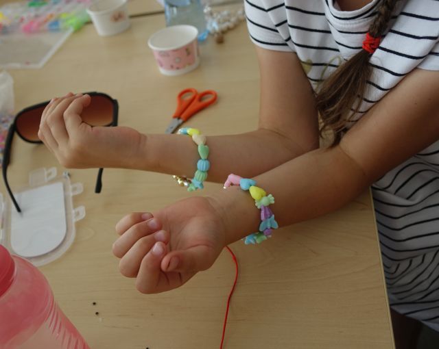 dwie dziecięce rączki prezentują wykonane przez siebie branzoletki z kolorowych koralików