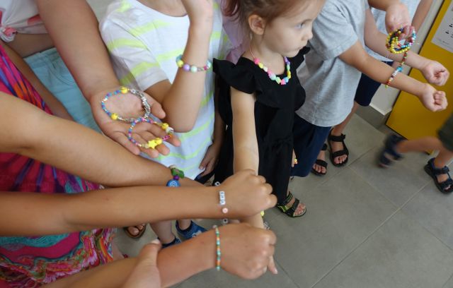 dzieci prezentują wykonane przez siebie kolorowe branzoletki z koralików