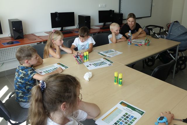 dzieci siedzą przy stolikach i wypełniają krzyżówki