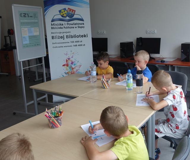 dzieci siedzą przy stolikach i wypełniają krzyżówki