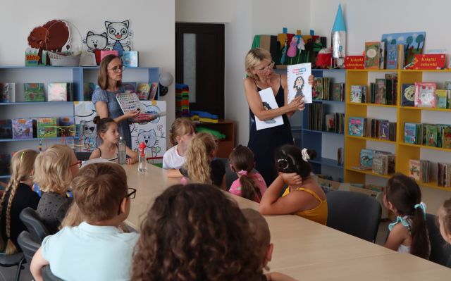 dzieci siedzą przy stole, przed nimi dwie kobiety pokazują ilustracje