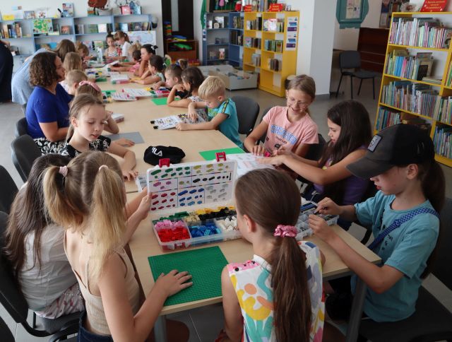 20 dzieci przy długim stole układa klocki LEGO