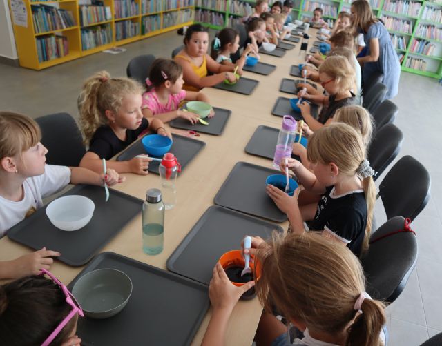 dzieci siedzą przy stołąch, przed nimi na siwych podkładkach małe miseczki