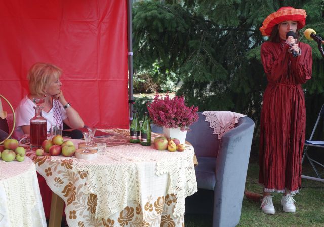 dziewczyna w czerwonej sukience śpiewa, aktorka siedzi i słucha