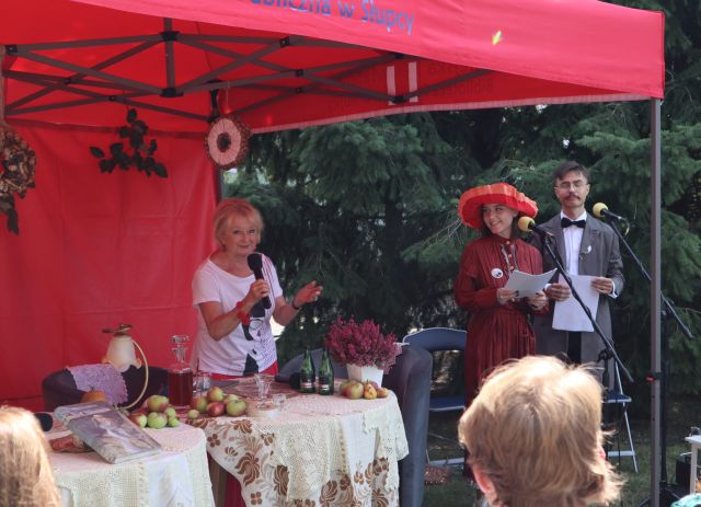 chłopak i dziewczyna w czerwonej sukience i kapeluszu patrzą w aktorkę mówiącą przez mikrofon