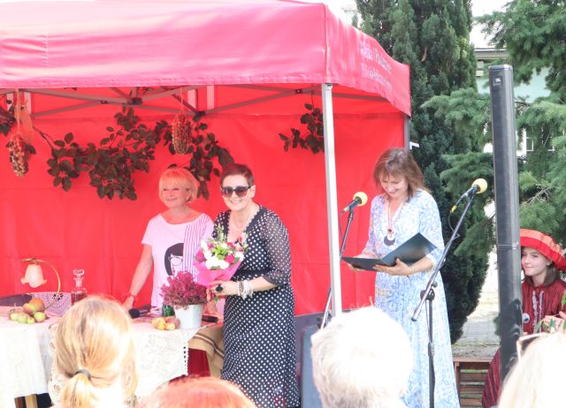 stoją aktorka, dyrektorka biblioteki przed mikrofonem iu kobieta z kwiatami