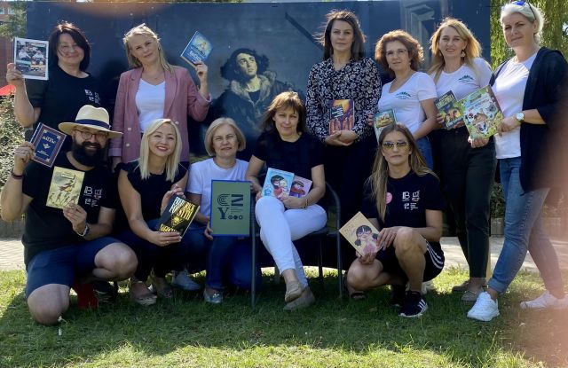 bibliotekarze z 5 bibliotek pozują do zdjęcia z książkami, w tle zdjęcie Kopernika