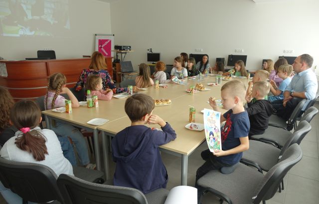 uczestnicy warsztató siedzą przy stołach przy poczęstunku oraz oglądają filmiki ze swoich warsztatów