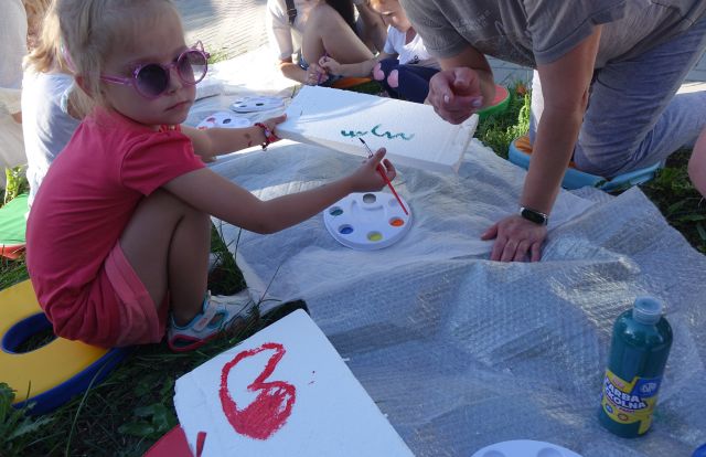 dzieci i opiekunowie malują po folii leżącej na trawie