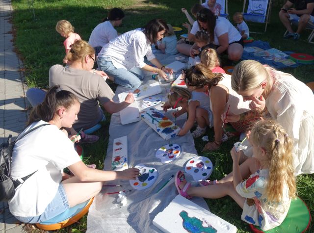 dzieci i opiekunowie malują po folii leżącej na trawie