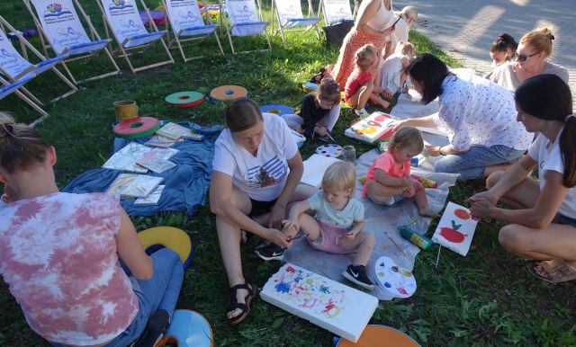 dzieci i opiekunowie malują po folii leżącej na trawie