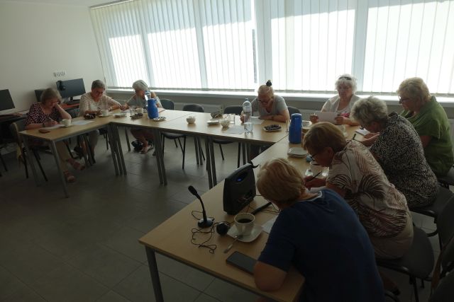 seniorki siedzą przy stołąch i wykonują ćwiczenia usprawniające mózg