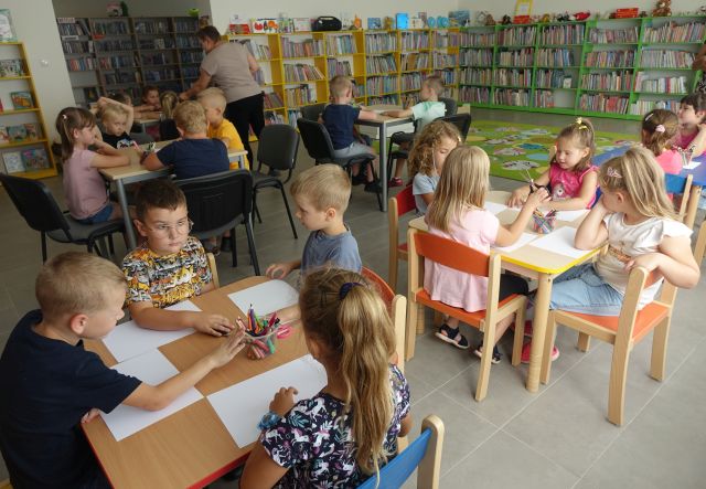 przedszkolaki siedzą przy stolikach i malują na kartkach