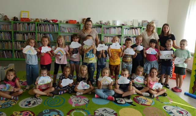 grupa przedszkolaków pozuje do zdjęcia z wykonanymi przez siebie ilustracjami, w tle regały z książkami