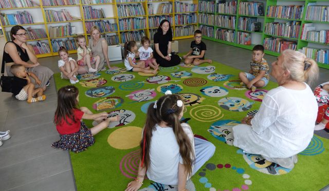 dzieci z rodzicami siedzą na kolorowym dywanie