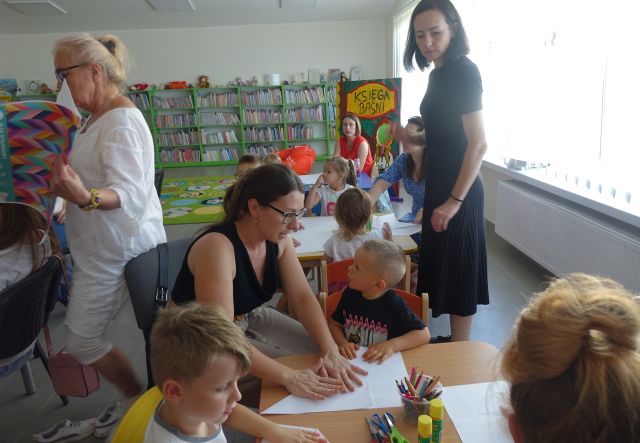 dzieci z rodzicami siedzą przy stolikach i malują