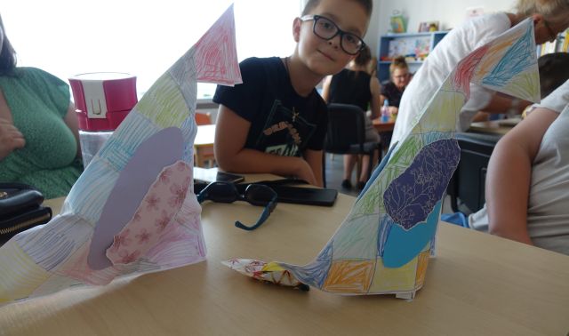 chłopiec prezentuje wykonane przez siebie kolorowe ptaki z papieru