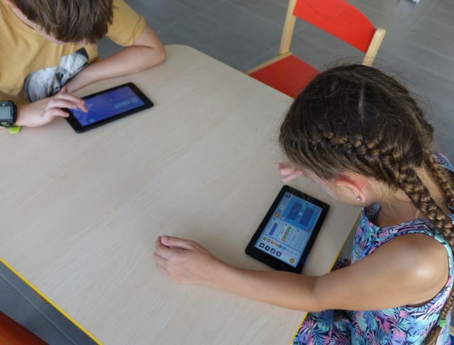 dziewczynka i chłopiec siedzą przy stoliku i grają na tablecie