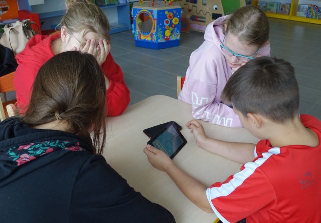 młodzież siedzi przy stole i gra na tablecie