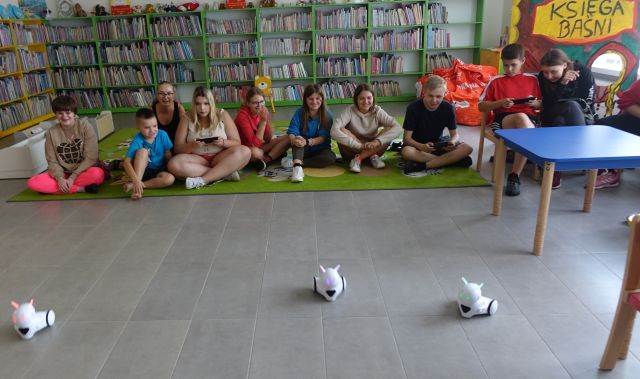 młodzież siedząca na kolorowym dywanie sterują przy użyciu tabletów robotami Photon