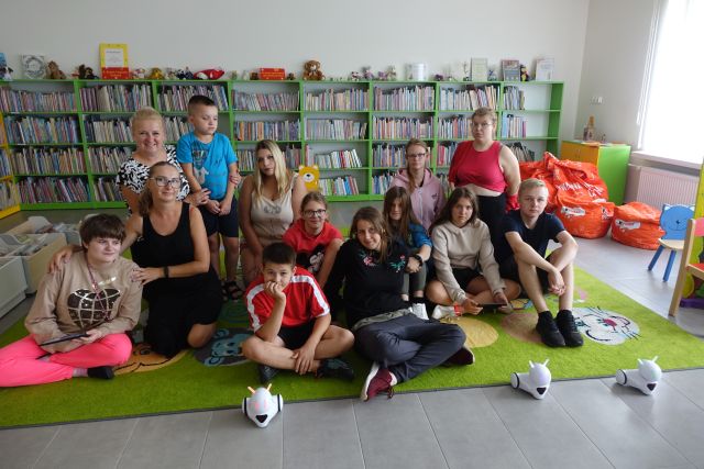 uczestnicy zajęć pozują do zdjęcia z robotami Photon, w tle regały z książkami