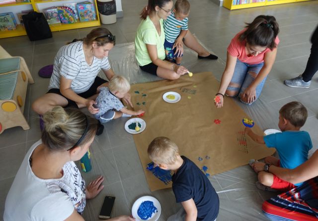 dzieci i rodzice malują na szarym papierze farbkami