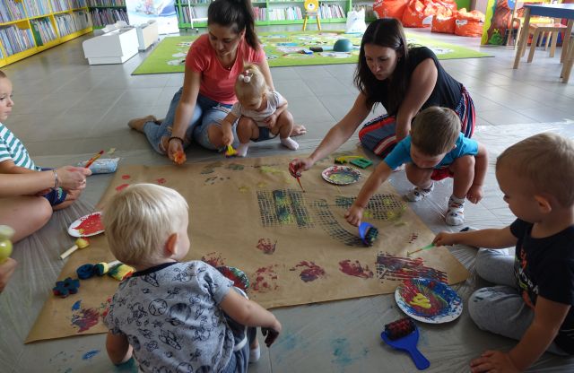 dzieci i rodzice odciskają na szarym papierze różne kształty gąbkami maczanymi w farbach