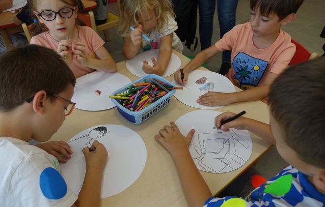 dzieci siedzą przy stoliku i malują na kołąch wyciętych z kartek