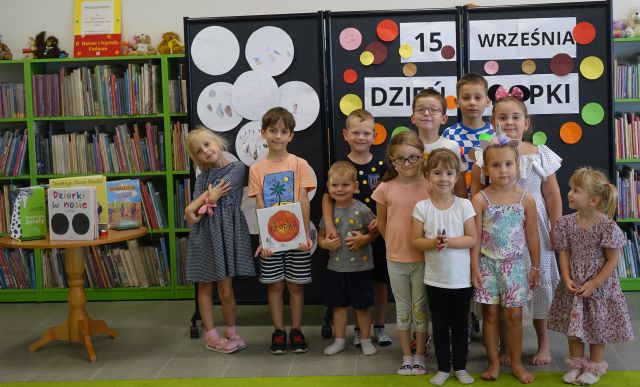 dzieci uczestniczące wwarsztatach pozują do zdjęcia, w tle szara plansza z nazwą dnia kropki i ilustracjami dzieci